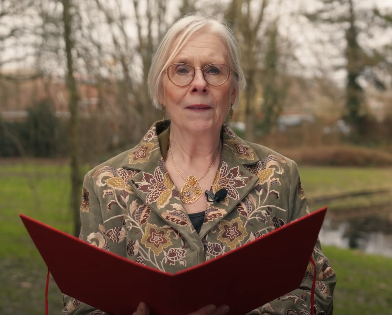 Kolet Janssen met rode kaft in een park, leest voor.