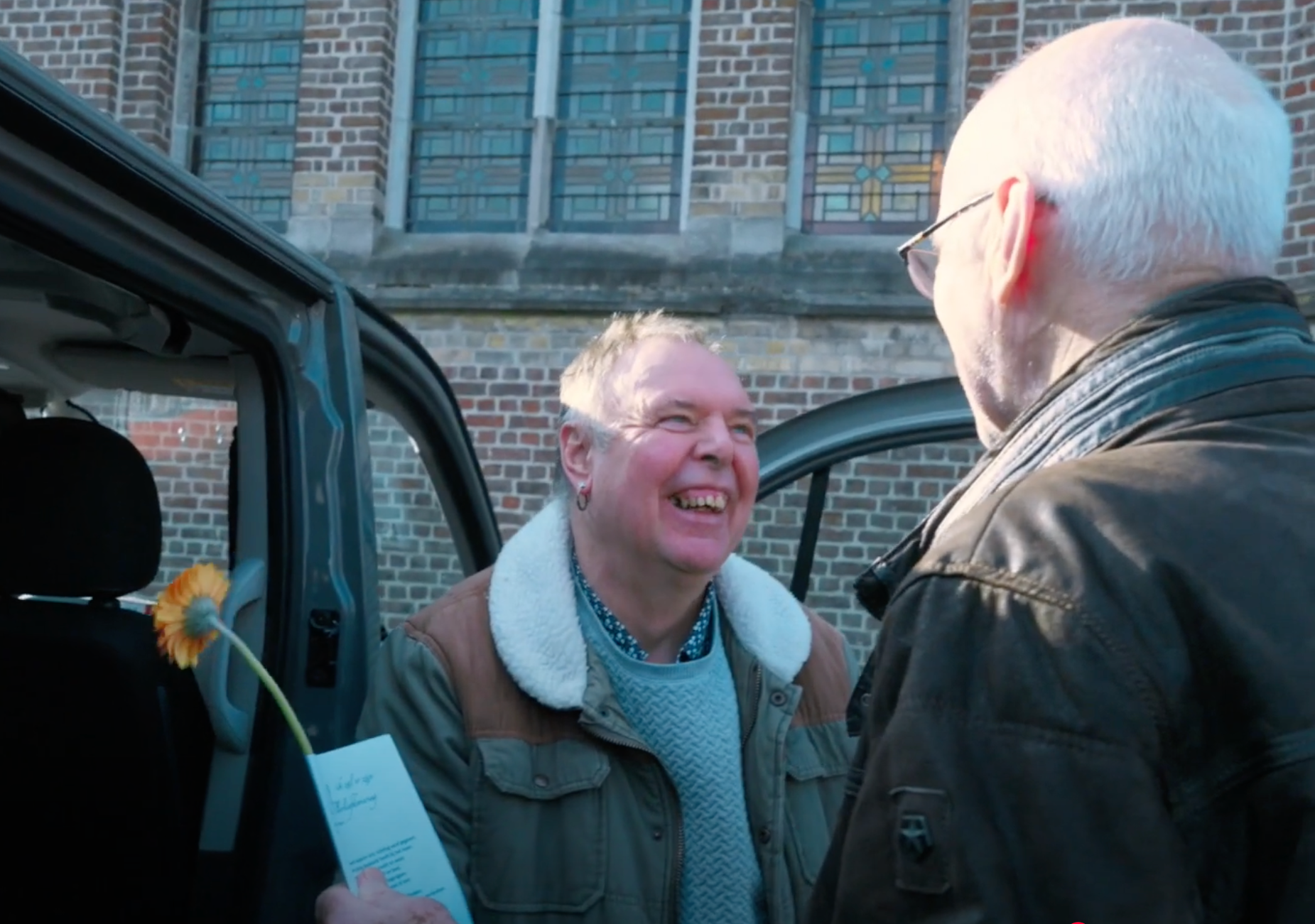Paul haalt met zijn busje mensen met een beperking op om samen naar de mis te gaan en krijgt een gulle lach van een van hen. 
