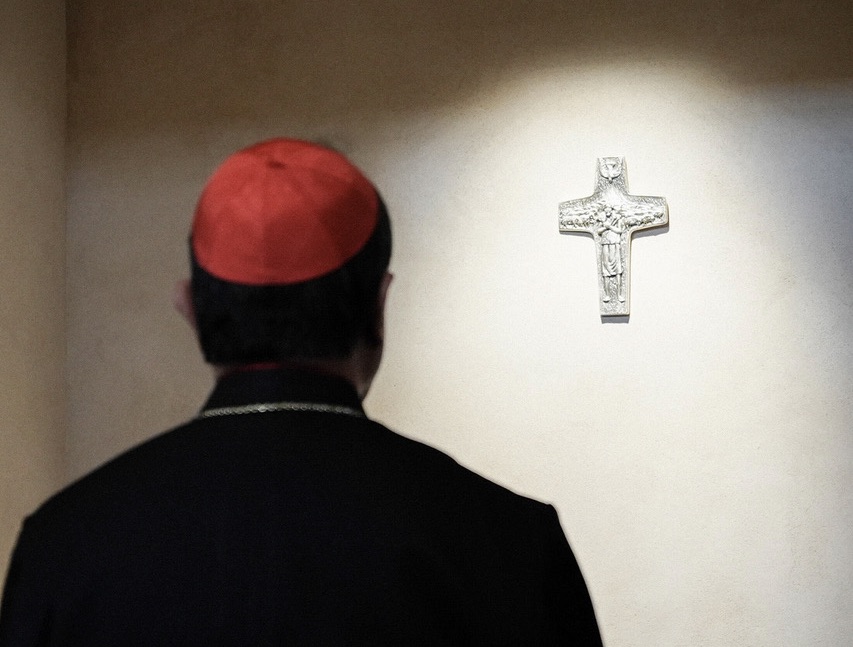 Een kardinaal in stilte bij het verlichte kruisje boven het graf van paus Franciscus.